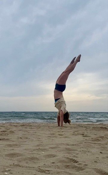 Handstand am Strand unter bewölktem Abendhimmel, dahinter das Meer
