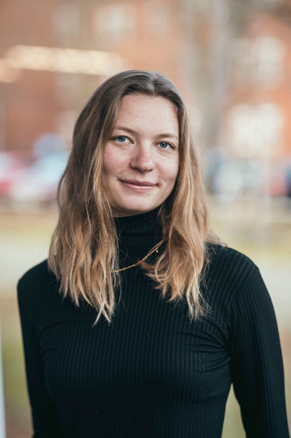 Porträt von Stephi Bünemann mit offenen blonden Haaren und schwarzem Rollkragenpullover, sie lächelt in die Kamera